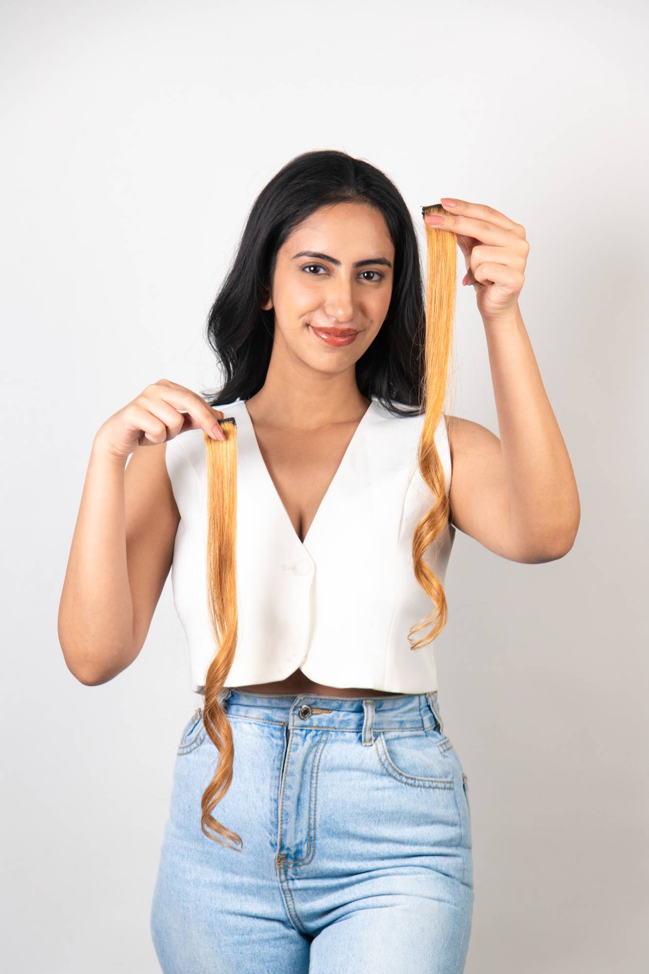 Indian model holding two Dolcy Blonde Clip-In Hair Streaks showing golden blonde color and clip attachment against dark black natural hair