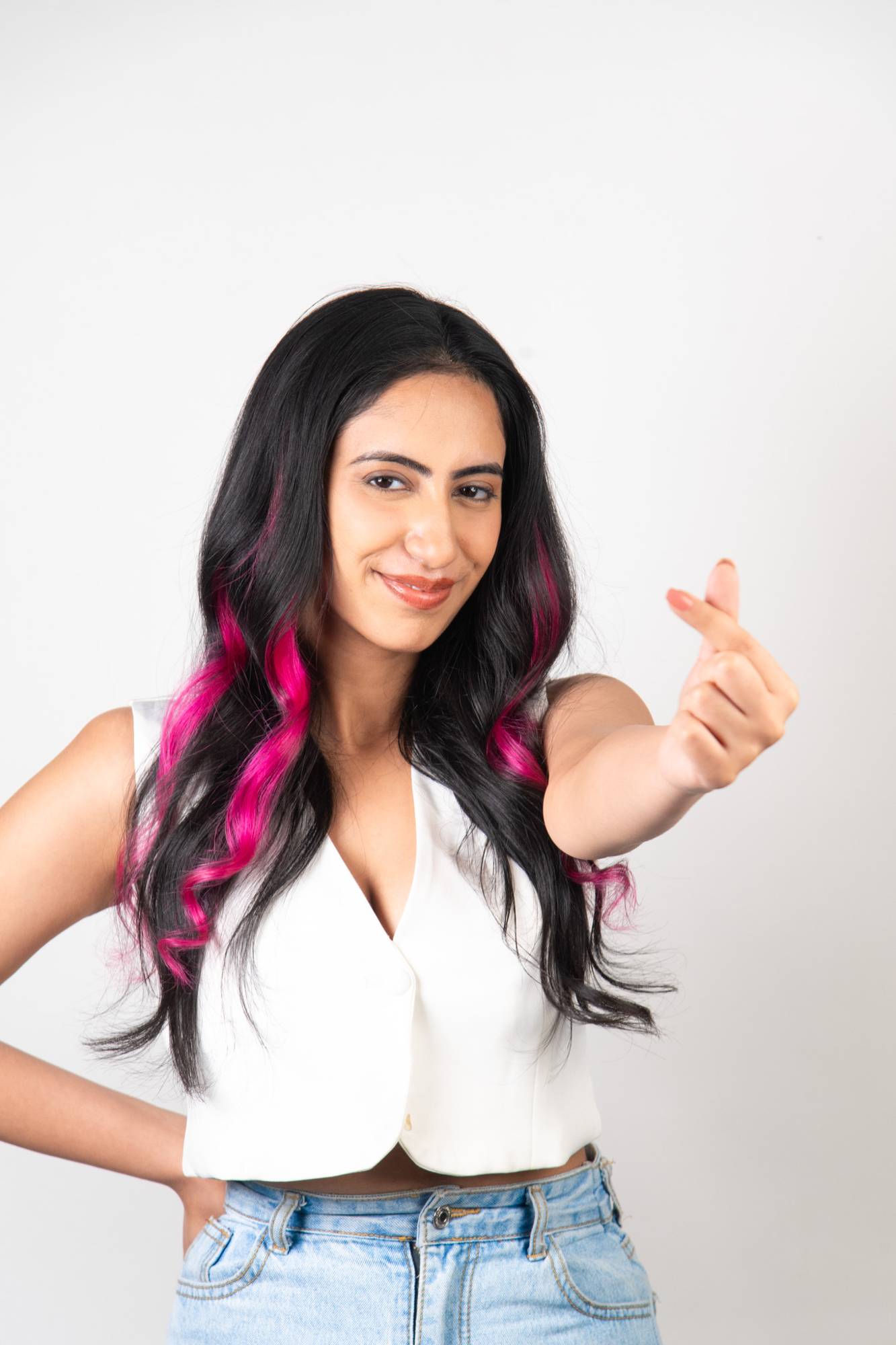 Confident model pointing to camera wearing Dolcy Neon Pink Clip-In Hair Streaks – bright neon pink streaks seamlessly blended into long dark black wavy hair